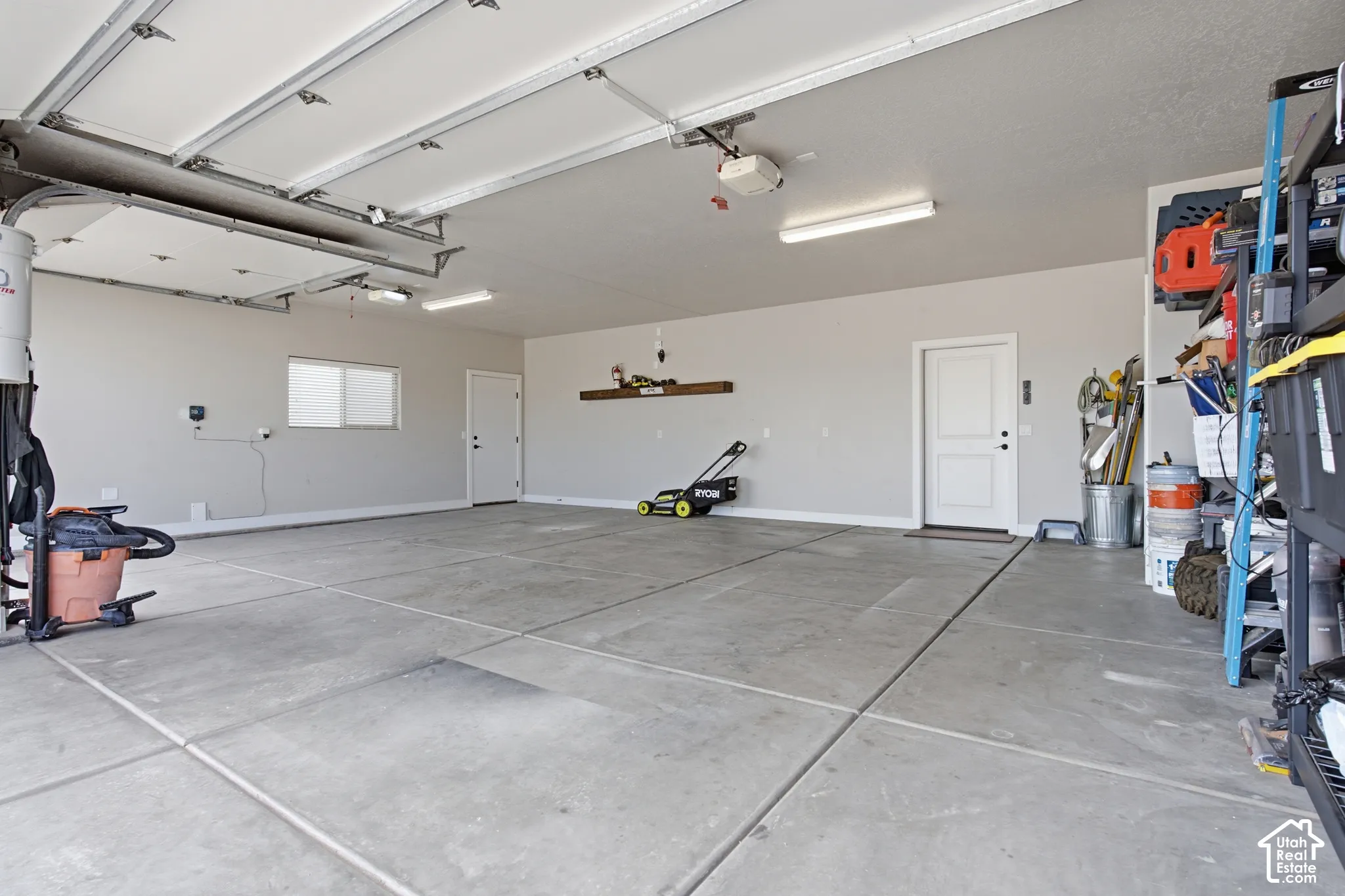 Spacious garage featuring concrete flooring, an overhead garage door, built-in overhead lighting, and a white access door