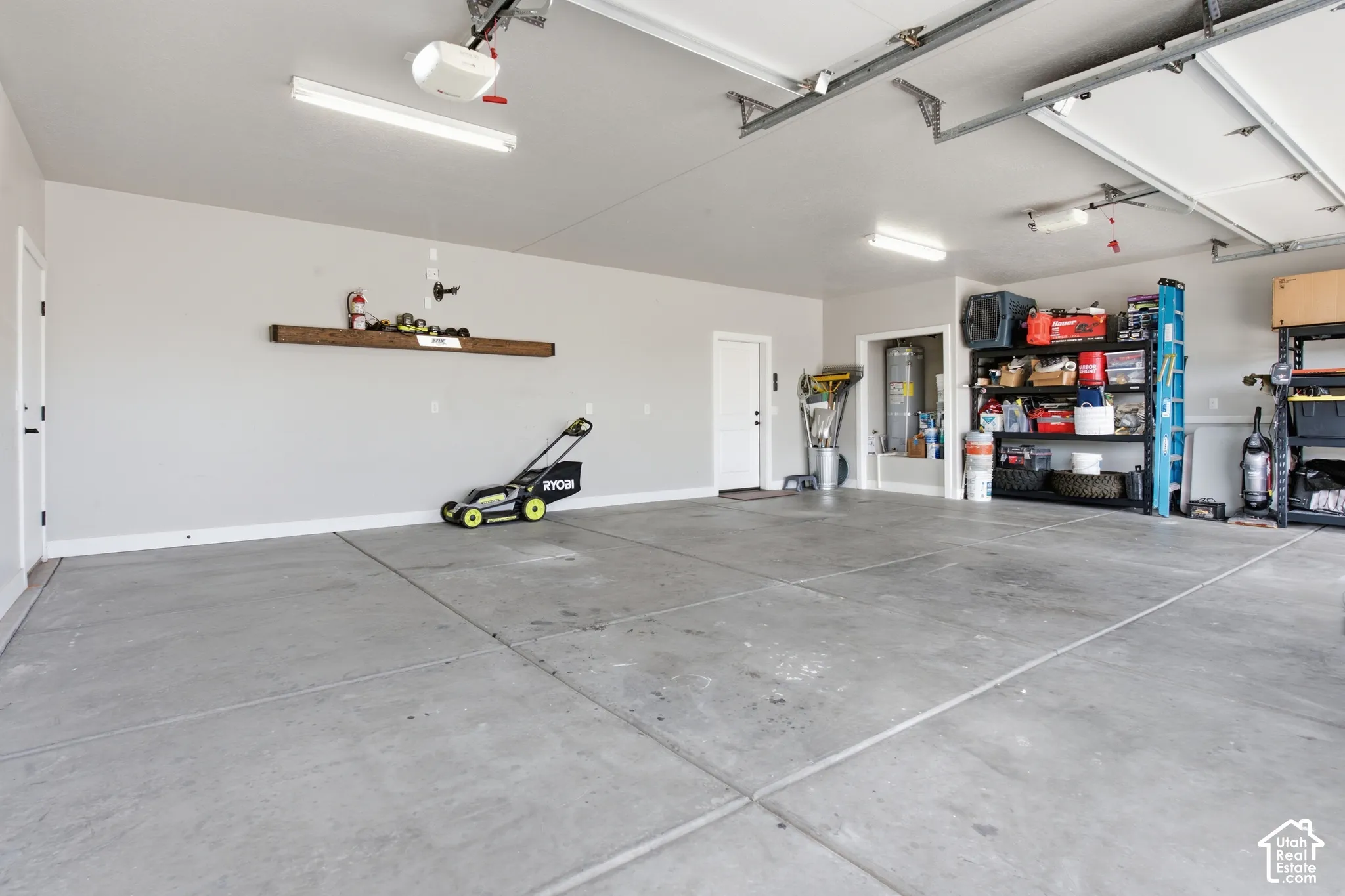 Spacious garage with concrete flooring, overhead fluorescent lighting, and a built-in wood-finish shelf