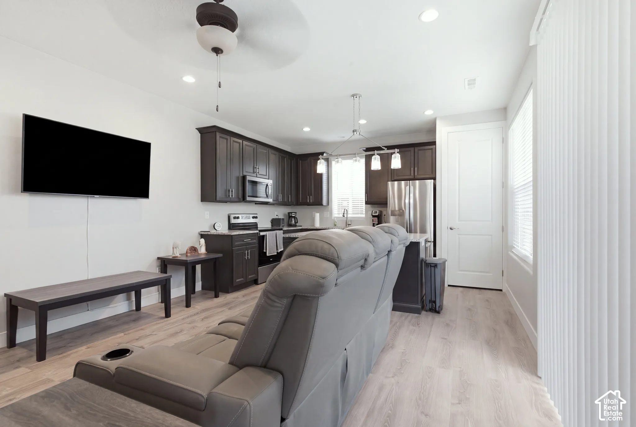Open-concept living space featuring wood-finish flooring, recessed lighting, a ceiling fan, dark wood cabinetry, and stainless steel appliances