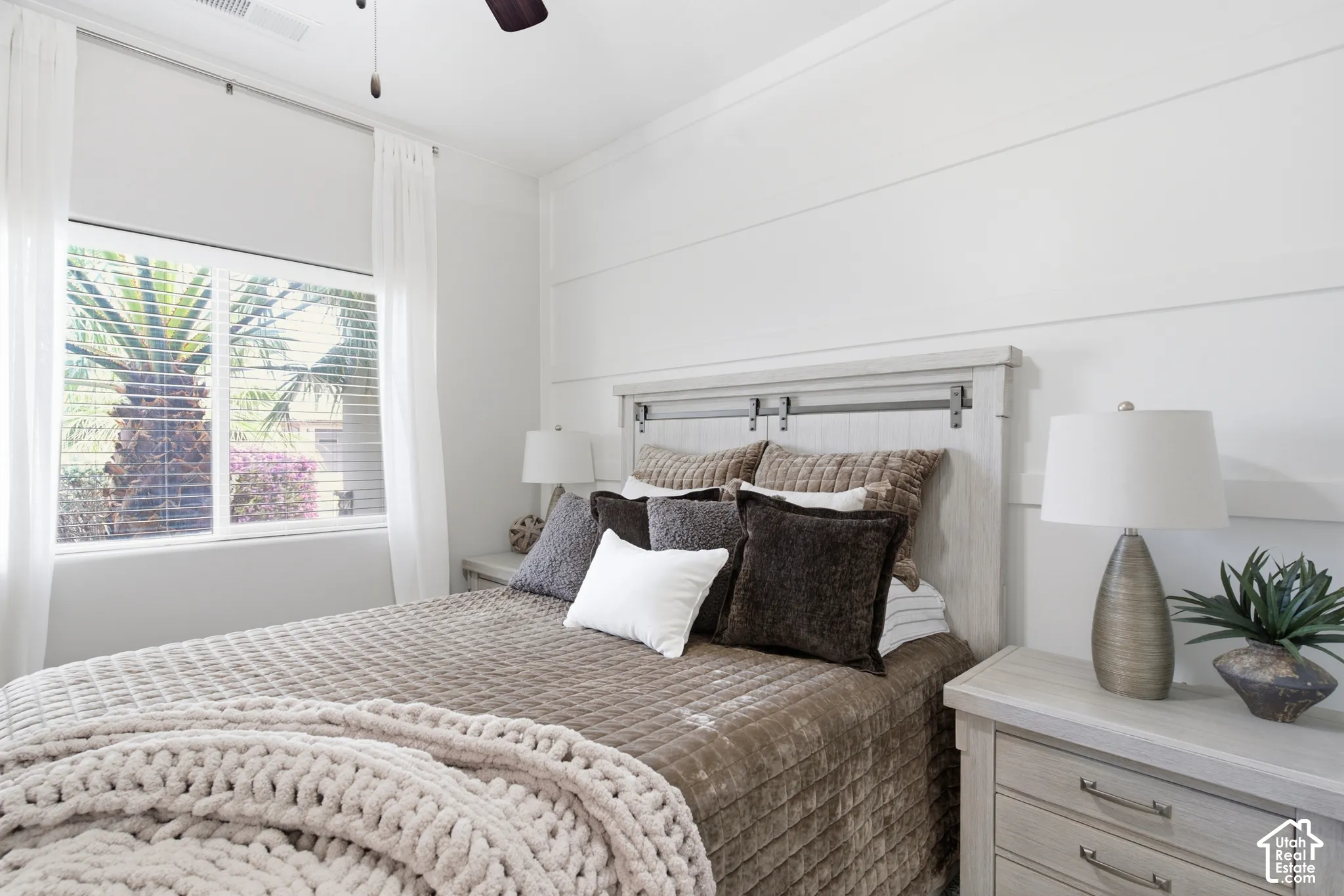 Shiplap accent wall, wood-finish headboard, window with blinds, ceiling fan, and built-in lighting