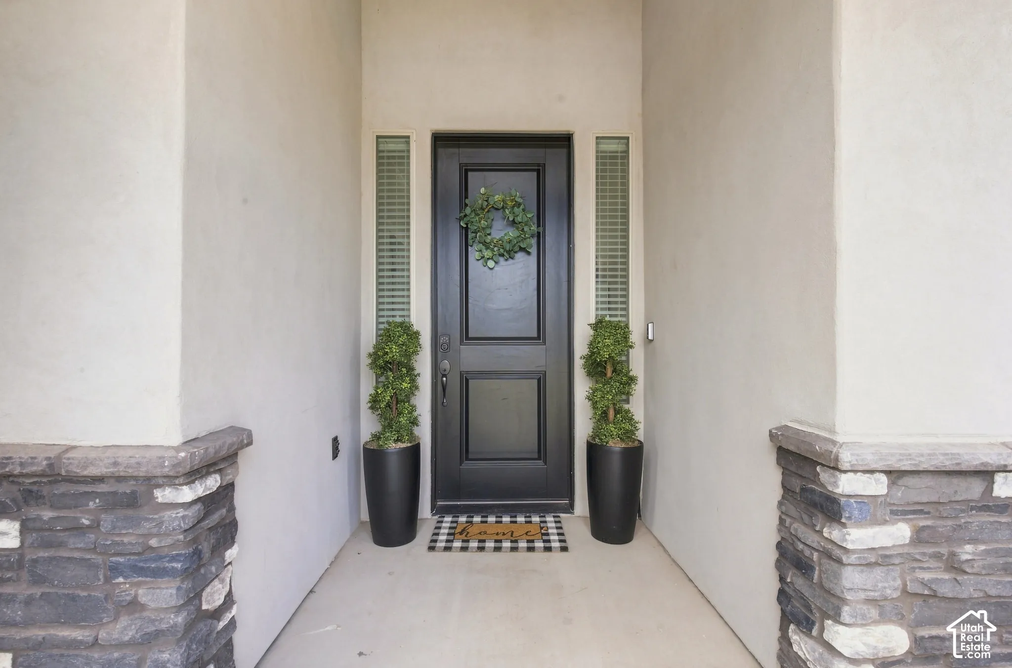 Entryway featuring a black panel door, vertical frosted sidelights, stucco walls, and stone veneer accents