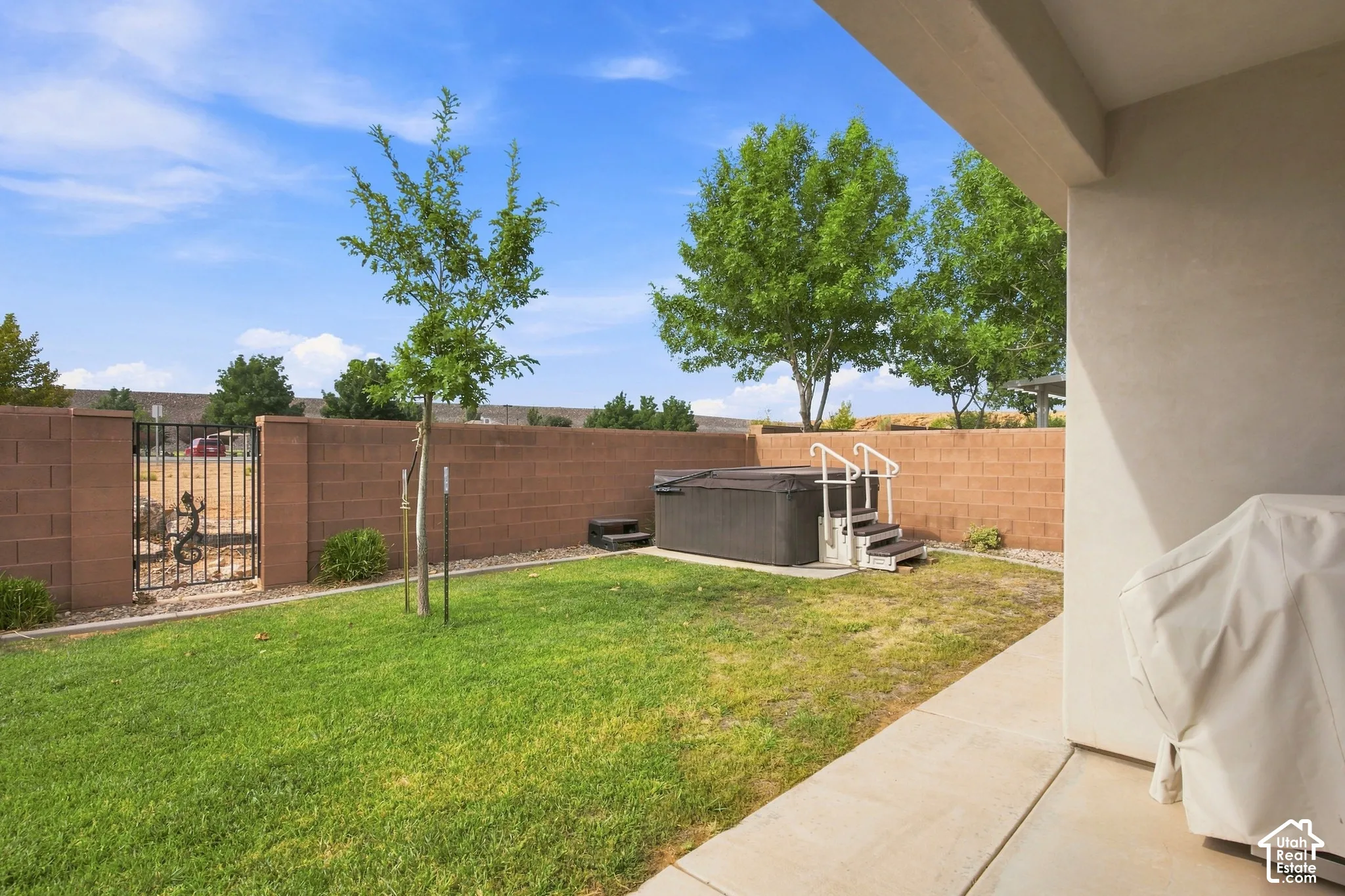 Enclosed backyard featuring a spa, concrete patio, and a block fence with a wrought iron gate