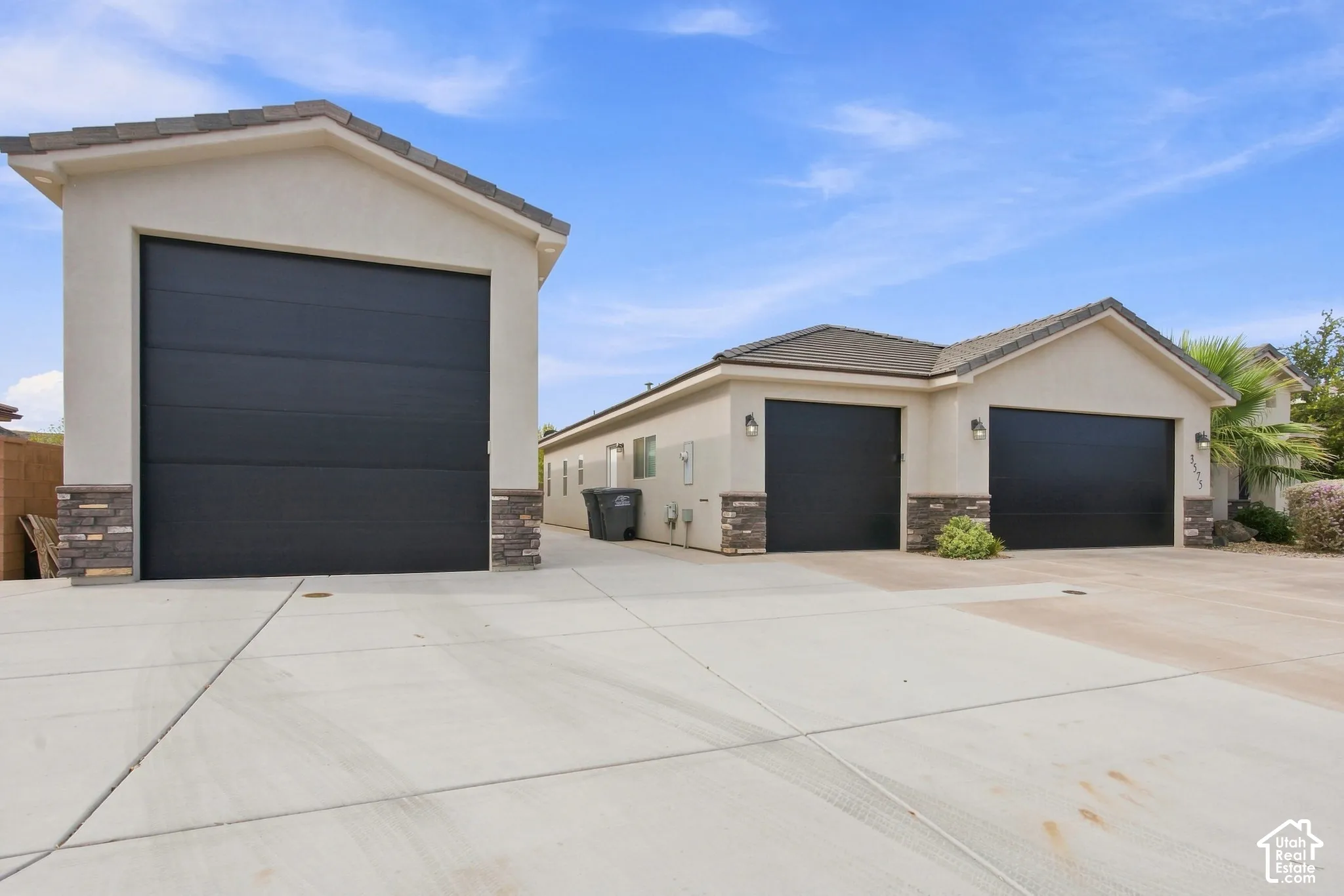 Stucco exterior with stone accents, multiple black garage doors, and a concrete driveway