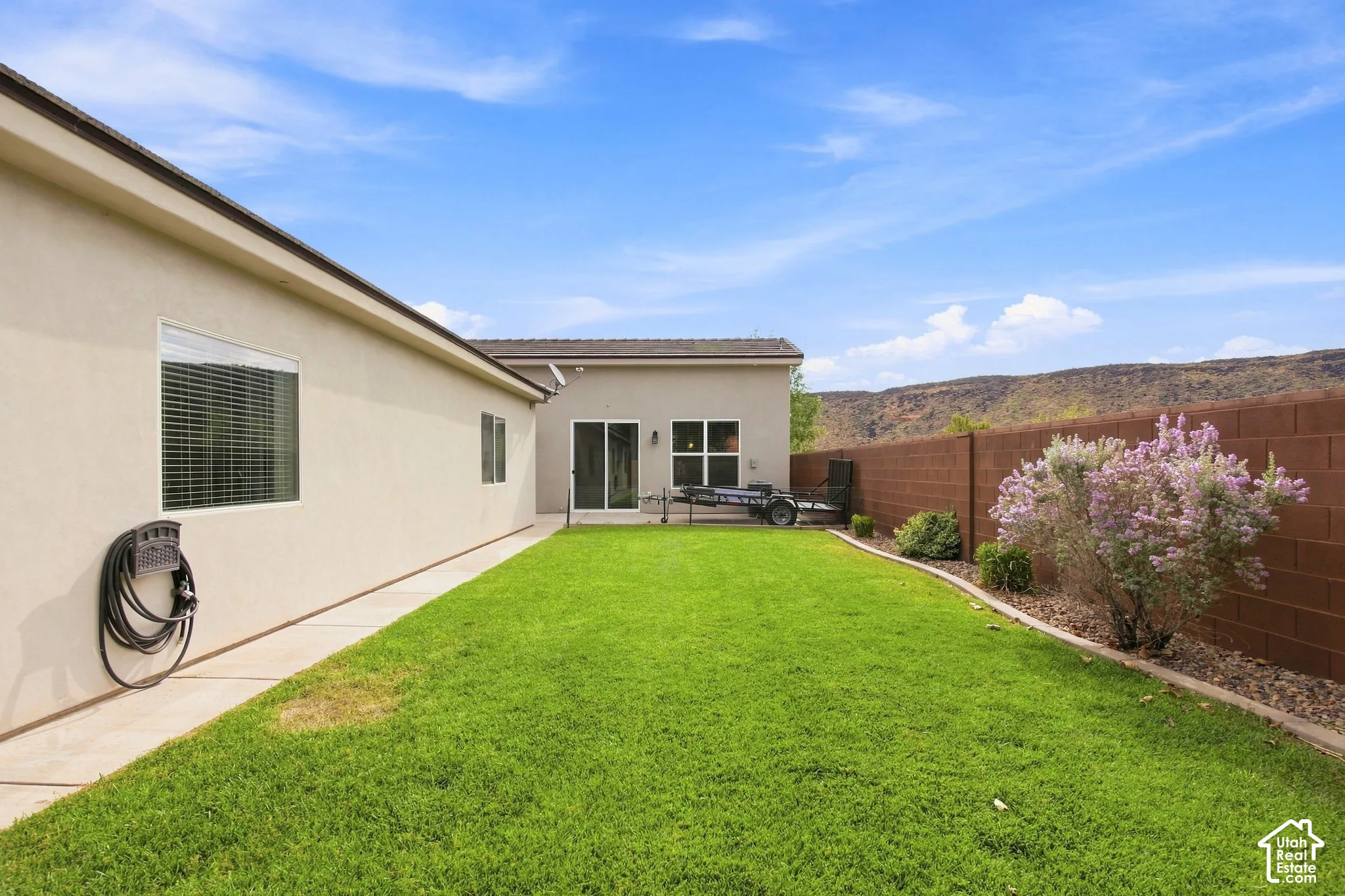 Expansive green lawn, concrete patio, sliding glass door access, perimeter block wall, and mature landscaping