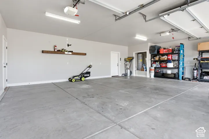 Spacious garage with concrete flooring, overhead fluorescent lighting, and a built-in wood-finish shelf