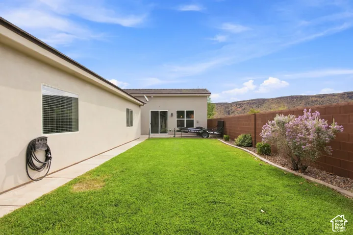 Expansive green lawn, concrete patio, sliding glass door access, perimeter block wall, and mature landscaping