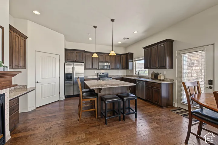 Wood-finish flooring, dark wood cabinetry, stainless steel appliances, granite countertops, and a kitchen island with seating