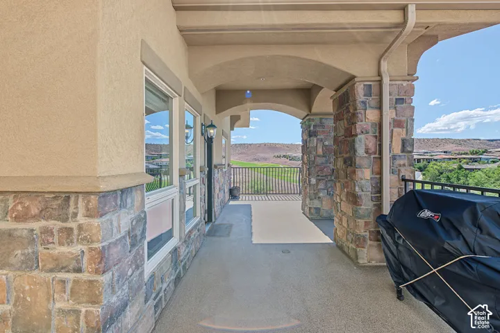 Covered outdoor patio with stone columns and stucco finish, featuring a durable concrete floor and a wrought iron railing