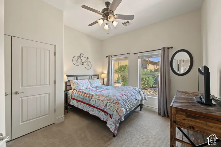 Vaulted ceiling with a ceiling fan, two windows providing natural light, carpeted flooring, and a paneled interior door