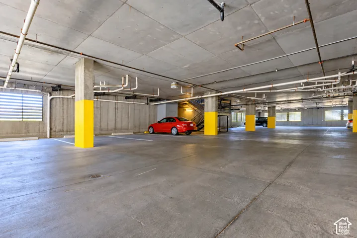 Concrete parking garage with multiple parking spaces, exposed ceiling pipes, and concrete support columns