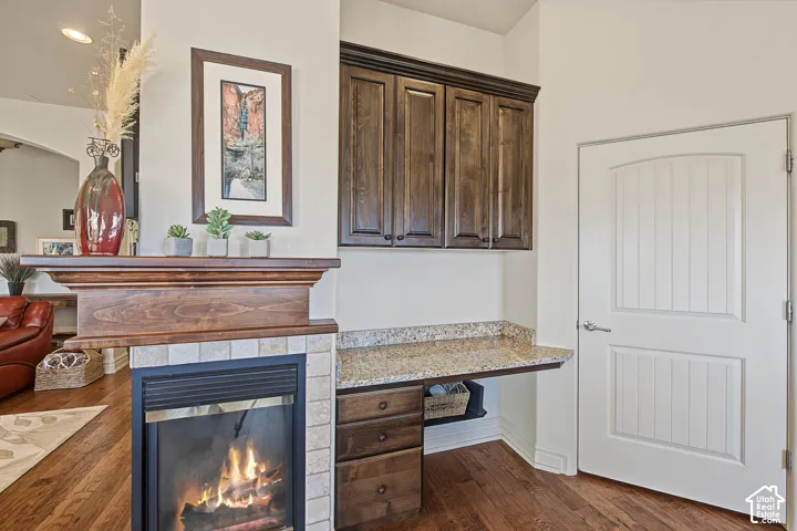 Wood-finish flooring, built-in fireplace with tile surround, wood mantel, built-in desk with stone countertop, and custom cabinetry