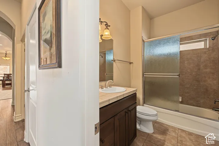 Wood-finish flooring, arched doorway, vanity with integrated sink, tile flooring, and a tiled shower/tub combination with sliding glass doors