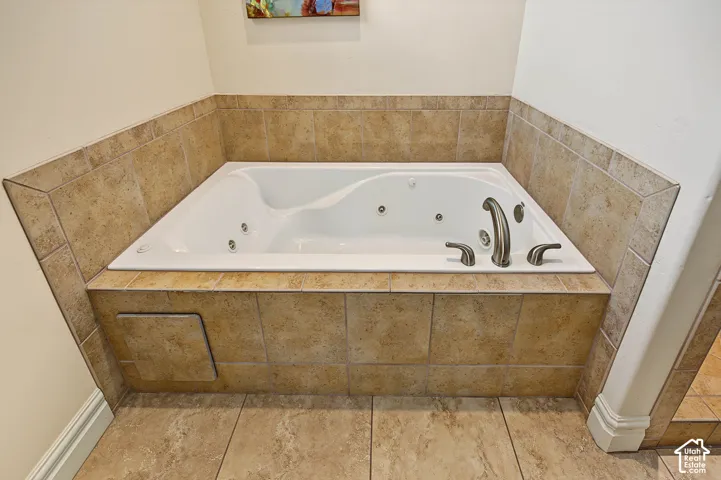 Jetted tub with brushed nickel fixtures, surrounded by neutral-toned tile and integrated access panel