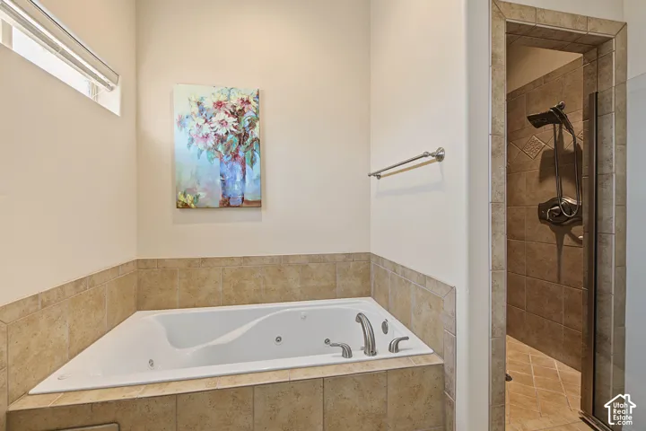 Jetted soaking tub with tile surround, walk-in shower with tile walls and floor, and a transom window