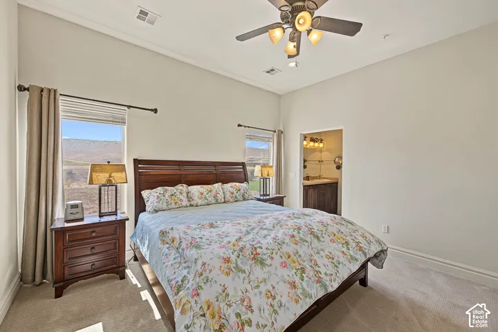 Vaulted ceiling, ceiling fan, carpet flooring, wood-finish bed frame, and an entry to a bathroom featuring a vanity