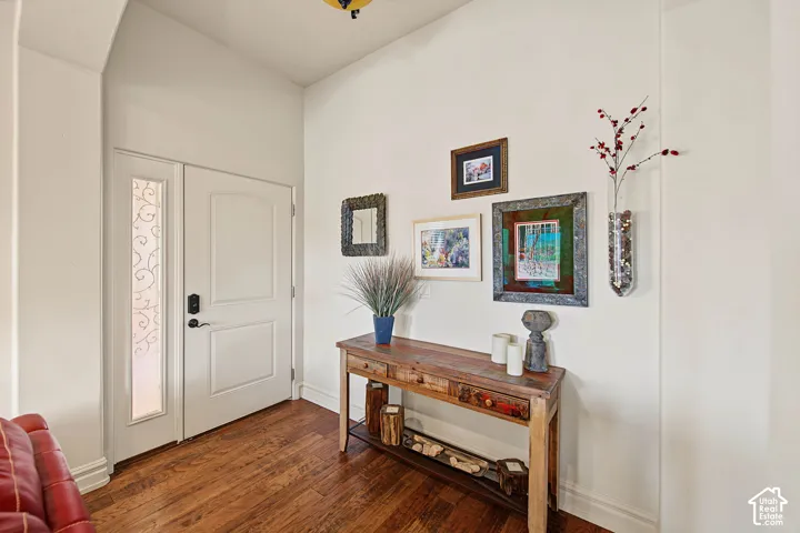 Hardwood flooring, white paneled entry door, decorative glass sidelight, vaulted ceiling, and white wall finishes