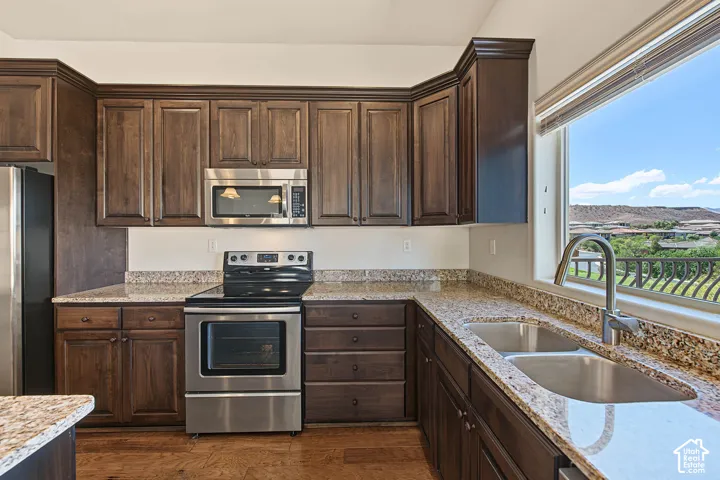 Kitchen featuring wood-finish flooring, dark wood cabinetry, granite countertops, and stainless steel appliances