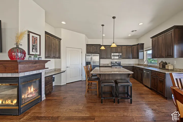 Corner fireplace with tile surround, wood-finish flooring, dark wood cabinetry, kitchen island with seating, and stainless steel appliances