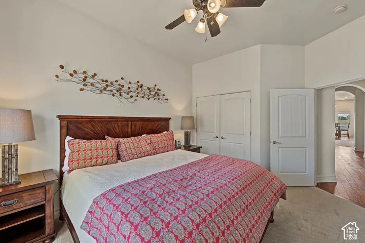 Vaulted ceiling, ceiling fan with integrated lighting, wood-finish headboard, archway entry, and white paneled doors