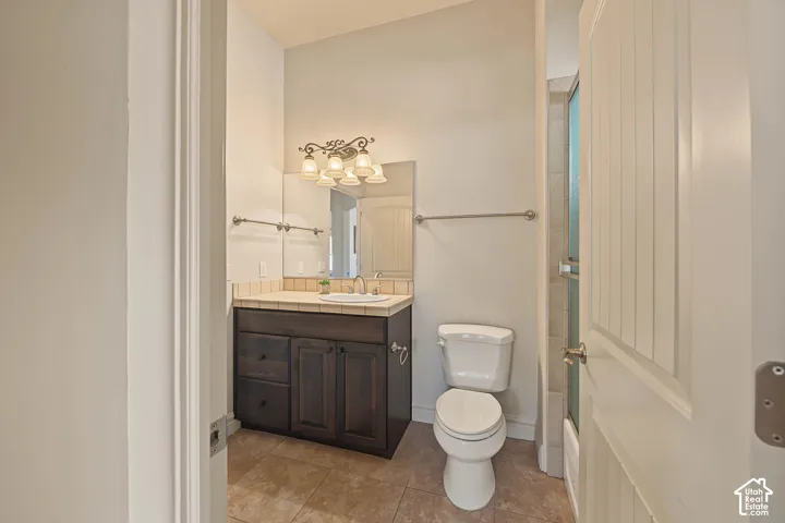 Bathroom featuring a dark wood-finish vanity with an integrated sink, tile countertop, and a decorative light fixture