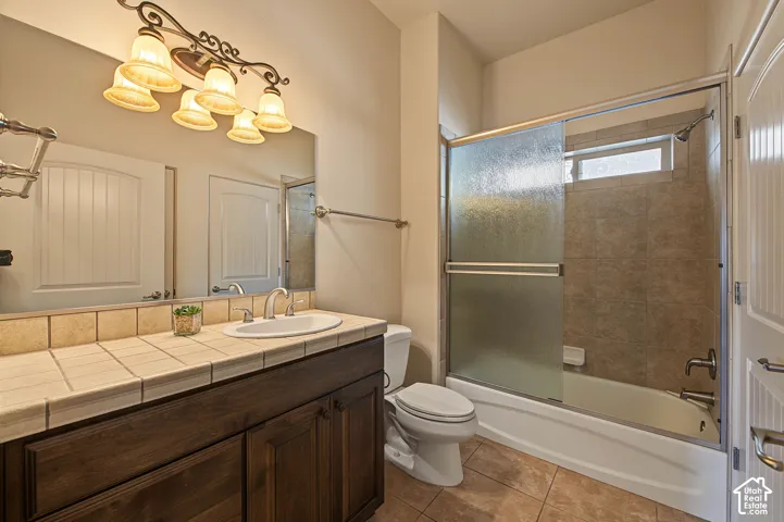 Wood-finish vanity with a tile countertop, integrated sink, and an overhead vanity light fixture