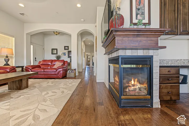 Wood-finish flooring throughout, featuring a tiled fireplace with a wood mantle, recessed lighting, and arched doorways
