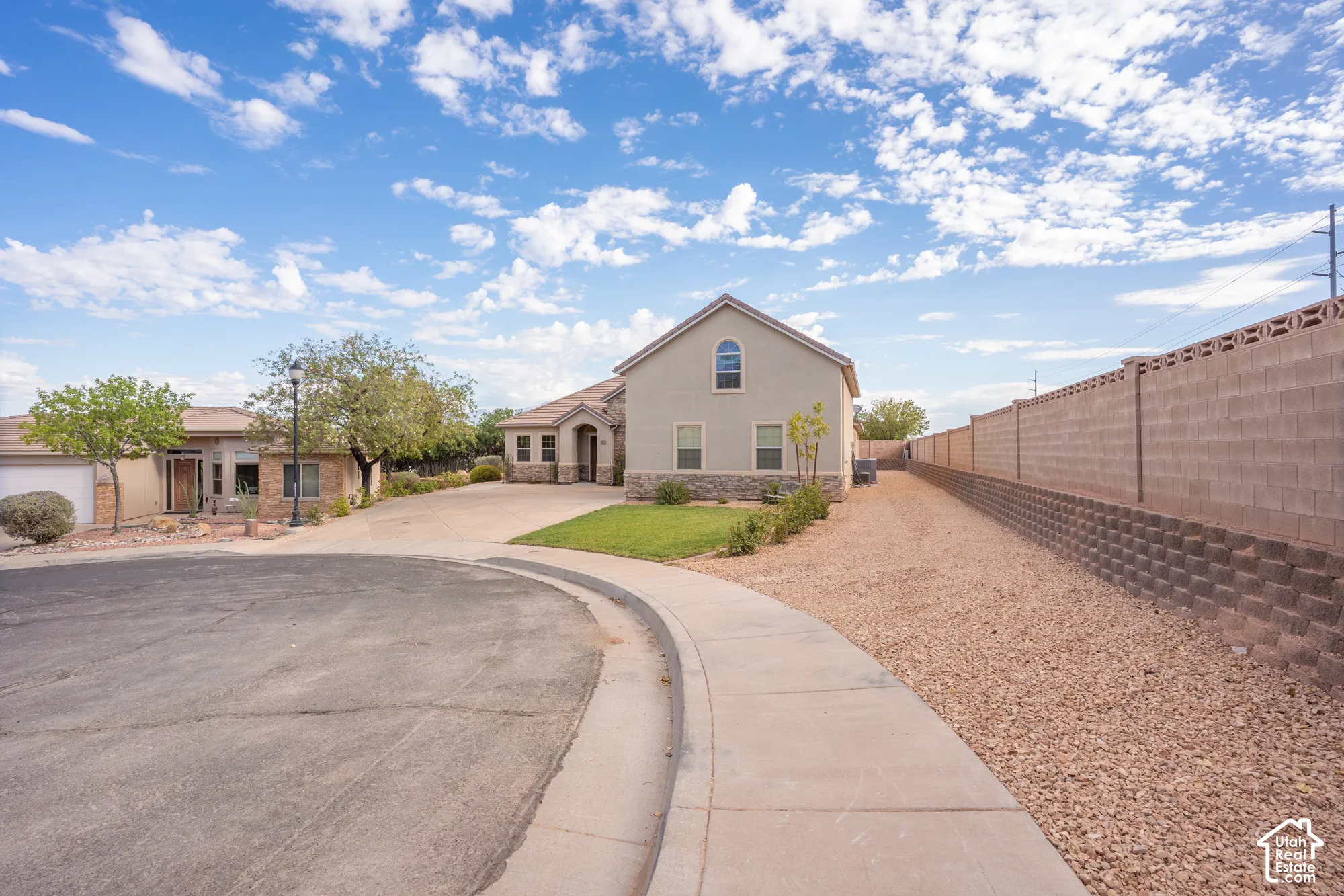 Stucco exterior with stone accenting, arched window, manicured lawn, concrete block perimeter wall, and gravel landscaping