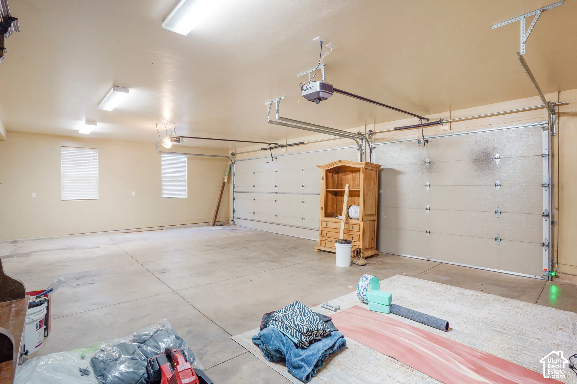Spacious garage featuring concrete flooring, multiple overhead light fixtures, two windows with blinds, and two automatic garage door openers