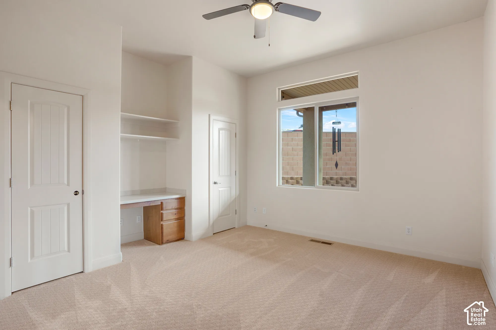 Recessed window with exterior wall framing, built-in desk with drawers, integrated shelving, and a ceiling fan with integrated lighting