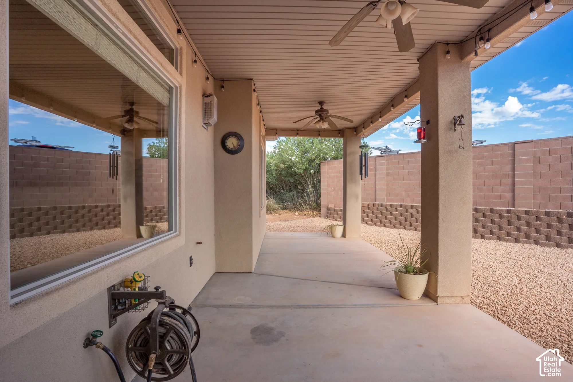 Covered patio with dual ceiling fans, concrete flooring, and a block wall with a decorative retaining wall