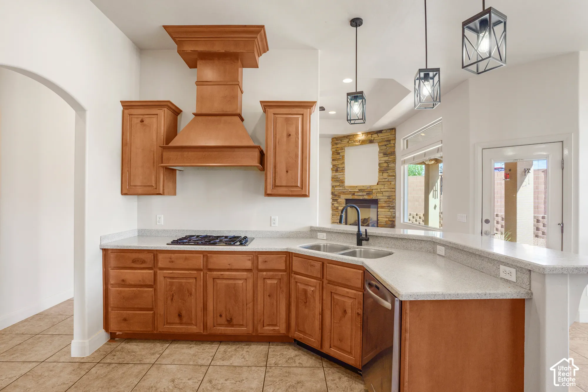 Kitchen featuring light wood cabinetry, light-colored countertops, a double basin sink with a matte black faucet, a built-in gas cooktop, and three pendant light fixtures