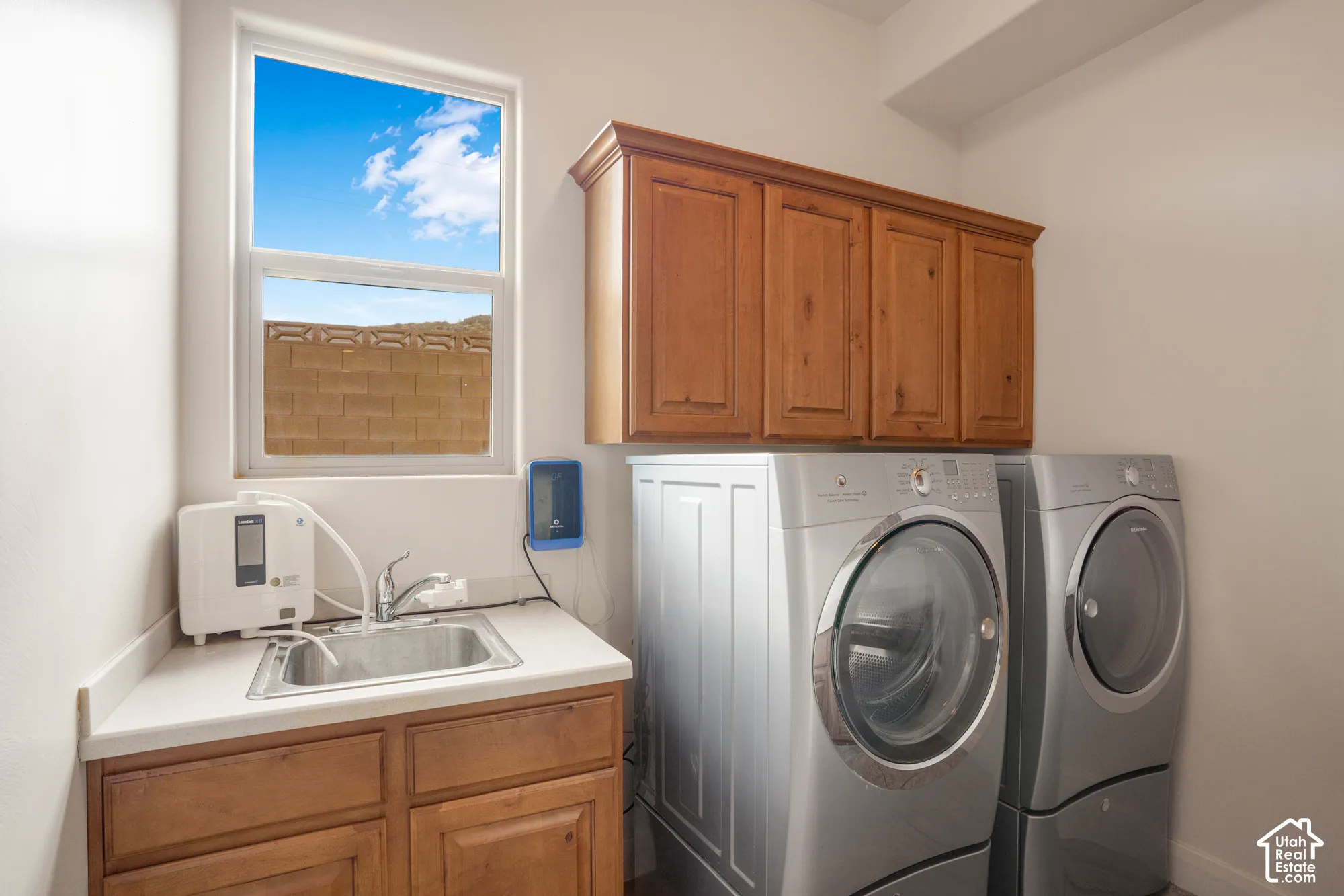Laundry area featuring wood-finish cabinetry, a utility sink with a stainless steel basin, and a window