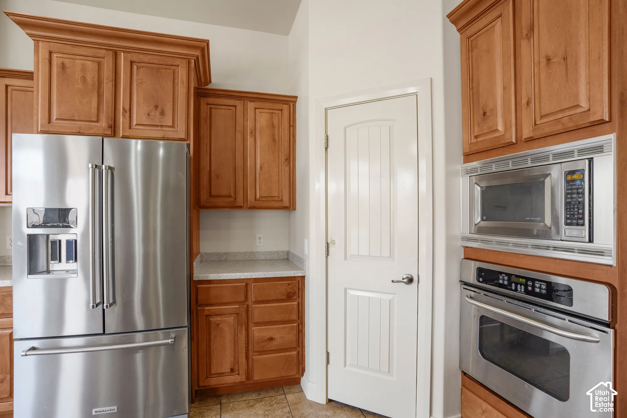 Stainless steel refrigerator, built-in microwave, wall oven, wooden cabinetry, and light-toned countertops