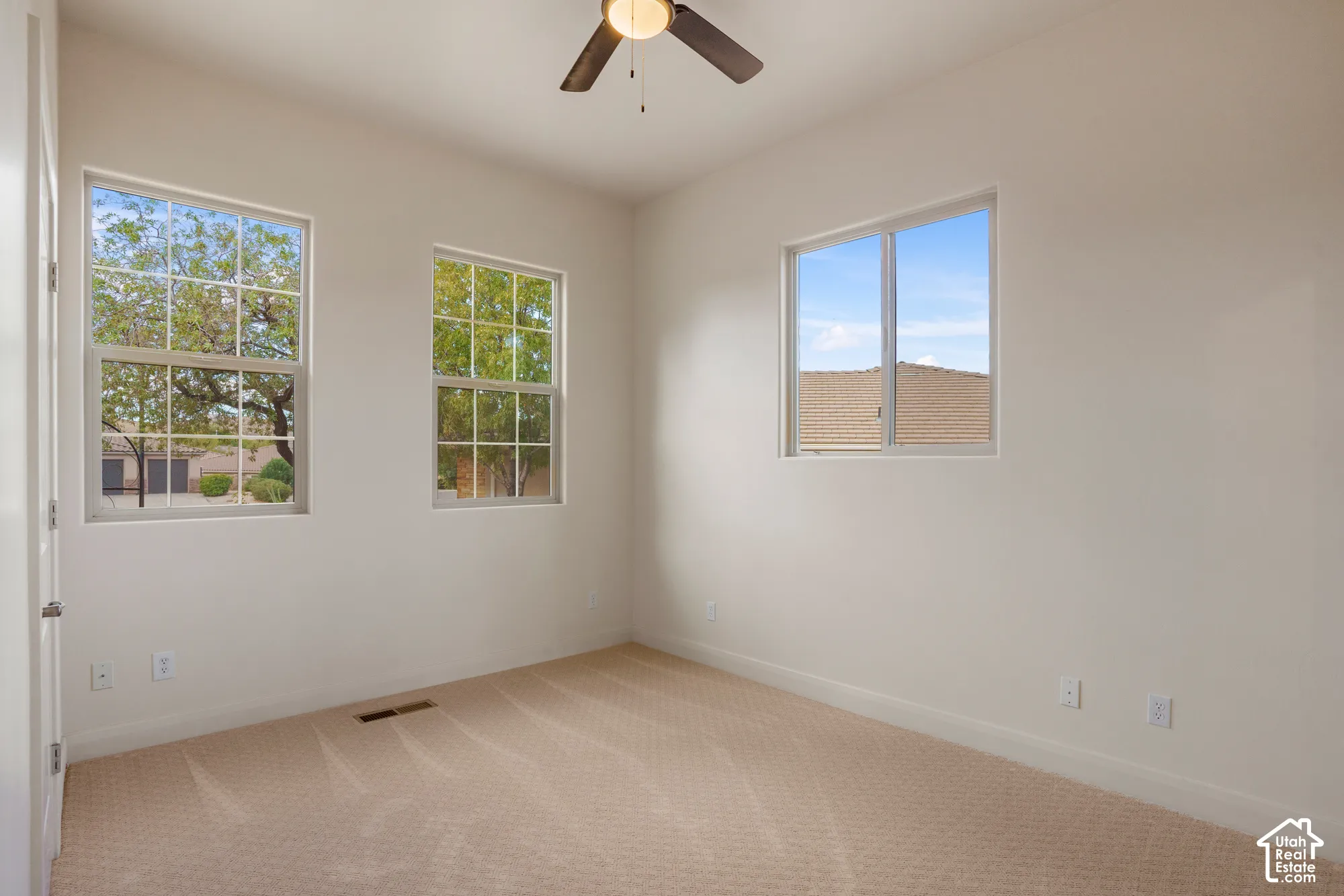 Room featuring light-toned carpeting, multiple windows, a ceiling fan, and neutral wall finishes