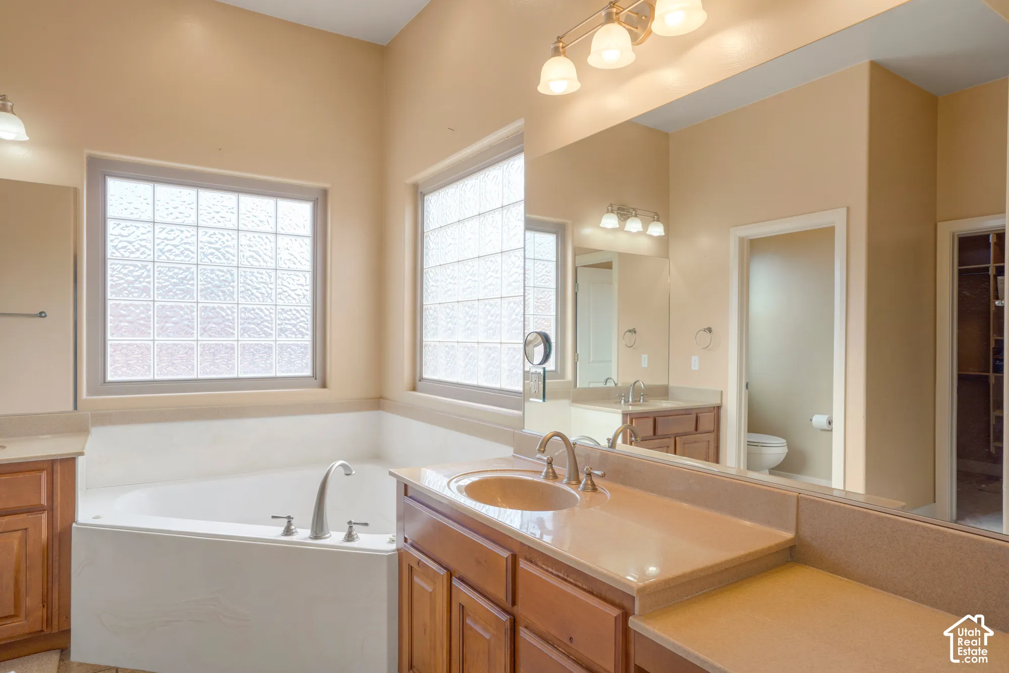 Spacious bathroom featuring a built-in bathtub, two glass block windows, dual vanities with integrated sinks, and ample wood-finish cabinetry