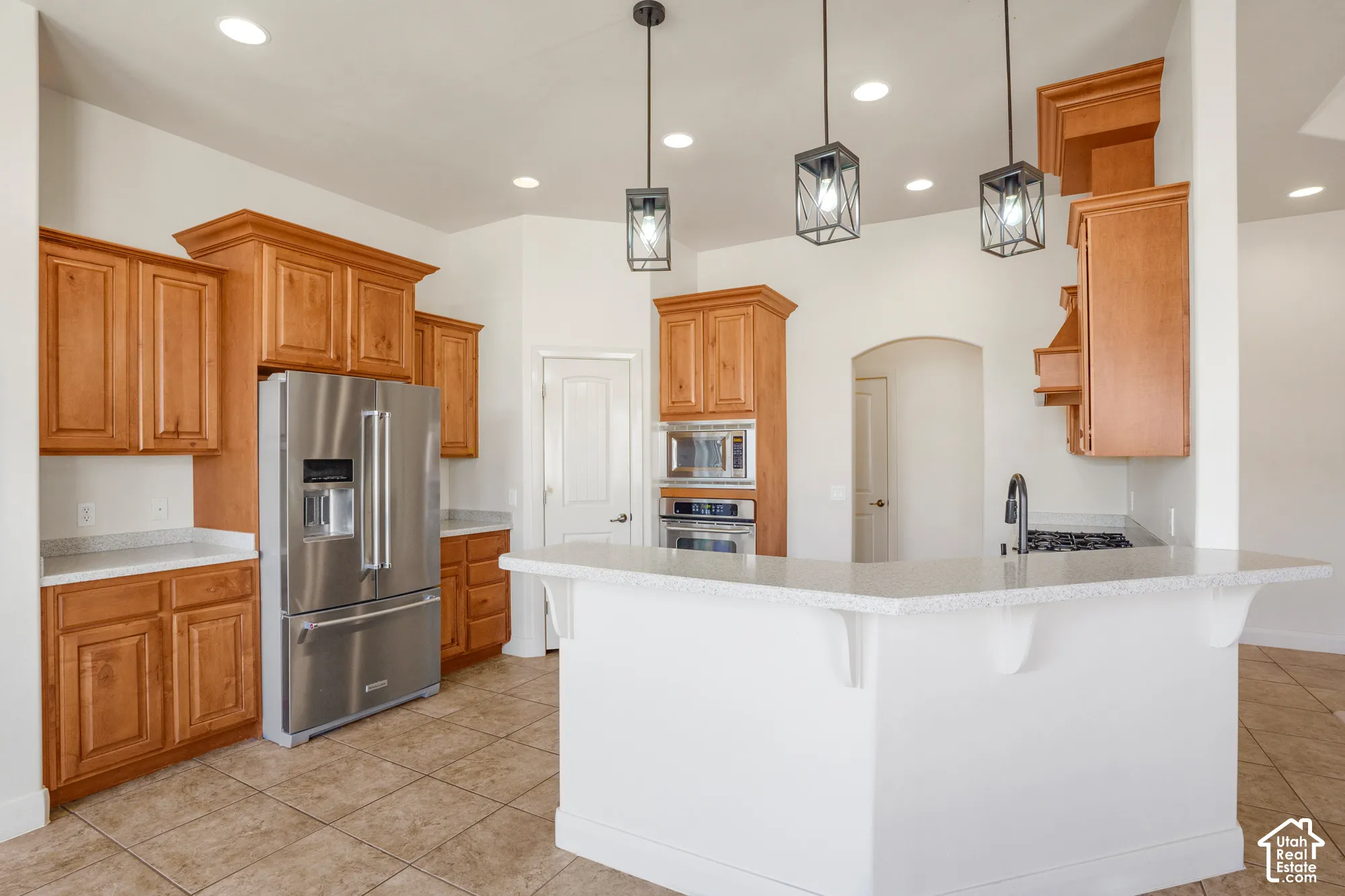 Stainless steel appliances, recessed ceiling lights, light wood-finish cabinetry, light-toned countertops, and floor tiles