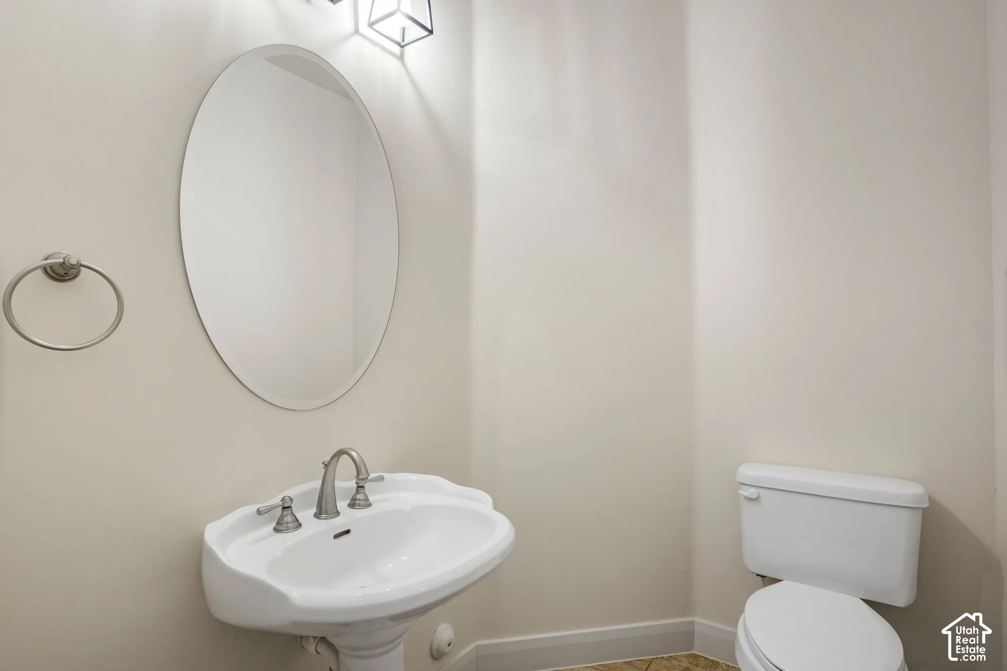 Pedestal sink, wall-mounted mirror, two-handle faucet, flush toilet, and wall-mounted light fixture