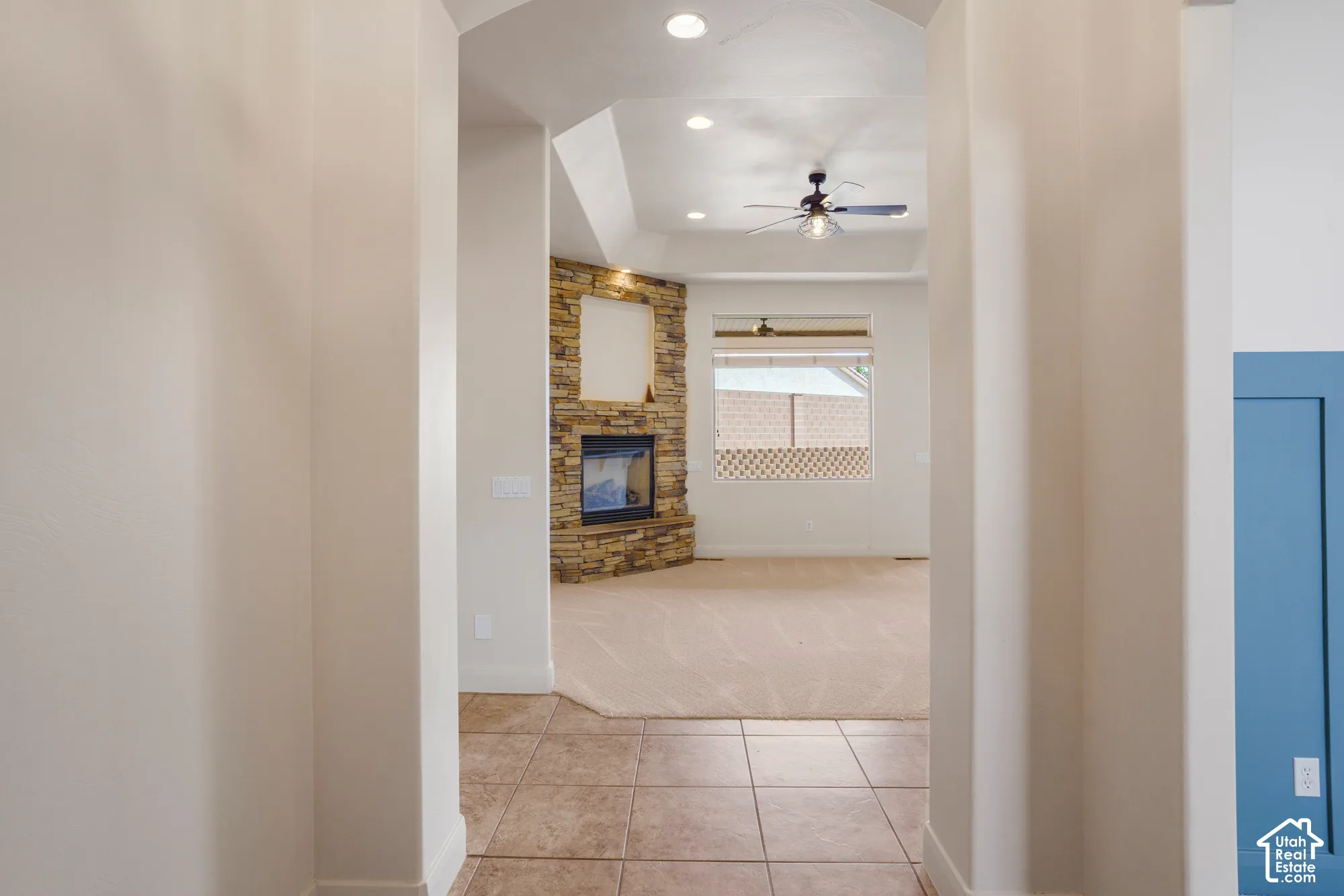 Tiled entryway with an arched ceiling leading to a living space featuring a stone-clad fireplace, carpet flooring, a ceiling fan, and recessed lighting