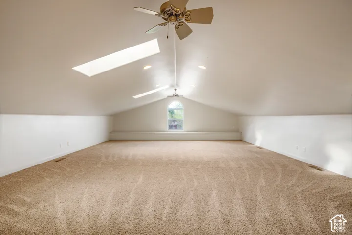 Expansive carpeted room featuring a vaulted ceiling, twin skylights, recessed lighting, ceiling fans, and an arched window