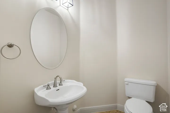 Pedestal sink, wall-mounted mirror, two-handle faucet, flush toilet, and wall-mounted light fixture
