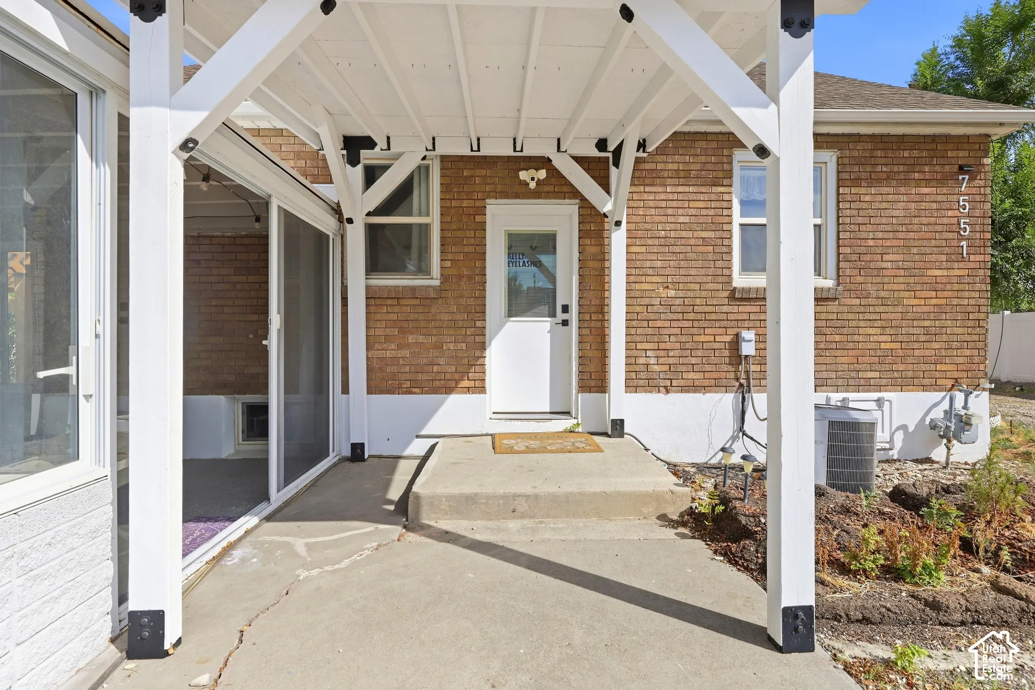 Covered concrete patio with white support beams and a brick exterior
