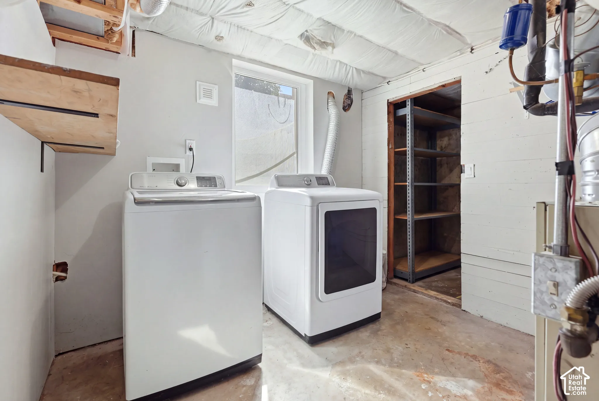 Utility area featuring a window, built-in shelving, concrete flooring, and an exposed ceiling