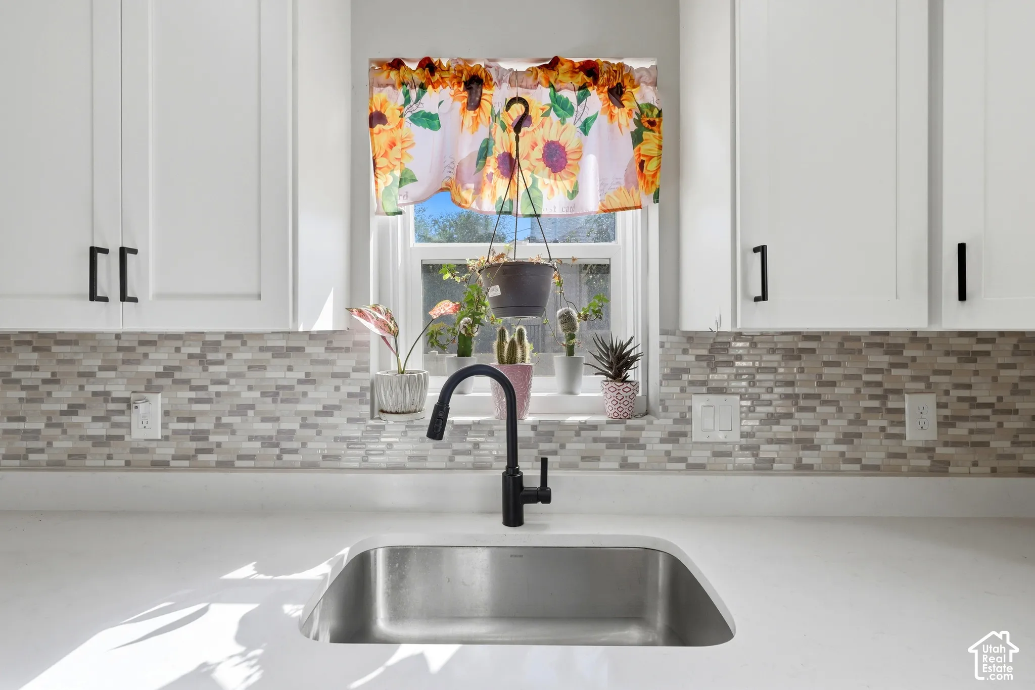 White shaker-style cabinetry with black hardware, mosaic tile backsplash, solid surface countertop, and an undermount stainless steel sink with a black gooseneck faucet