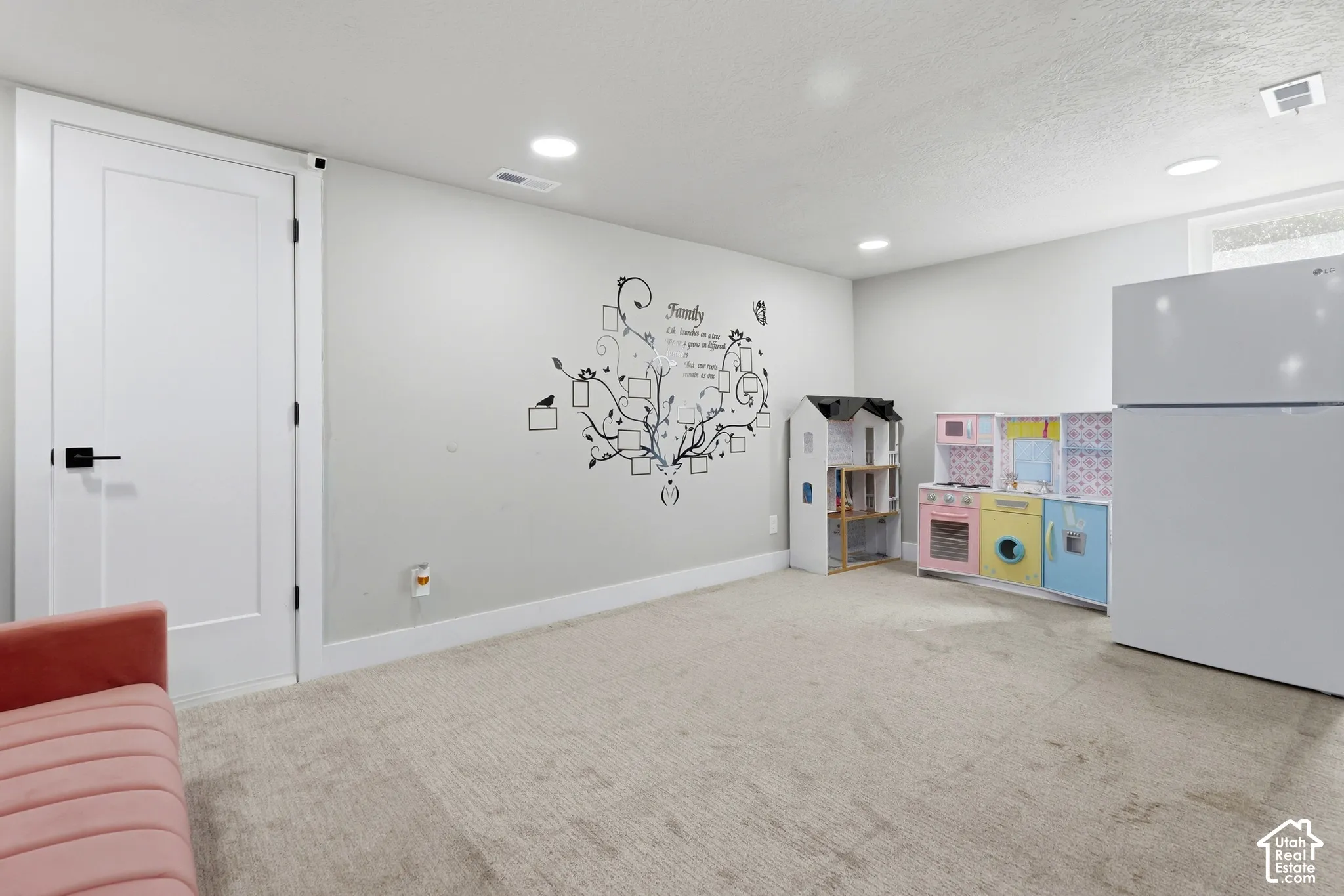Recessed lighting illuminates a spacious room featuring light-colored carpeting, a contemporary interior door with black hardware, and a window providing natural light
