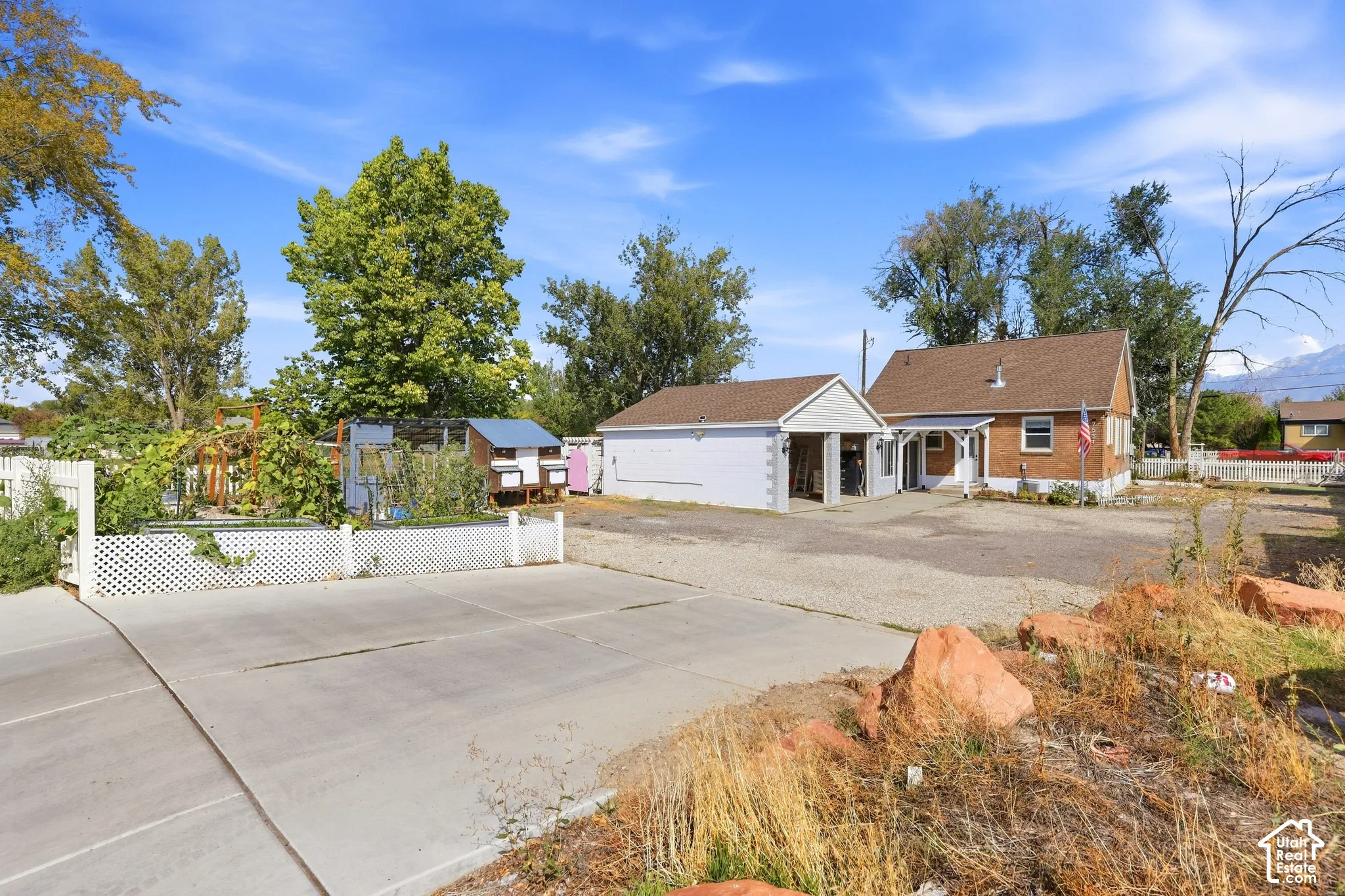 Brick exterior residence featuring a detached garage with an attached carport, a concrete driveway, and a fenced garden area
