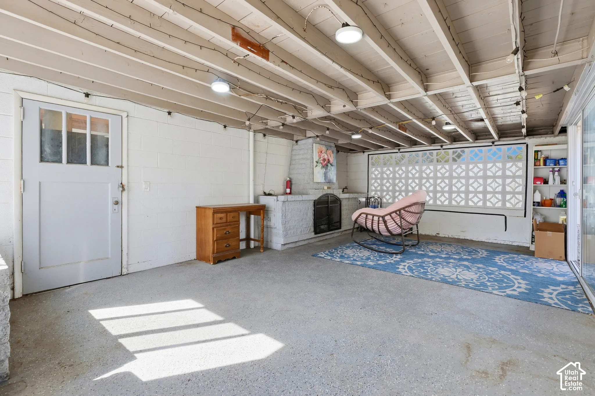 Covered patio area featuring a concrete floor, exposed wood beam ceiling, and a built-in fireplace with a hearth