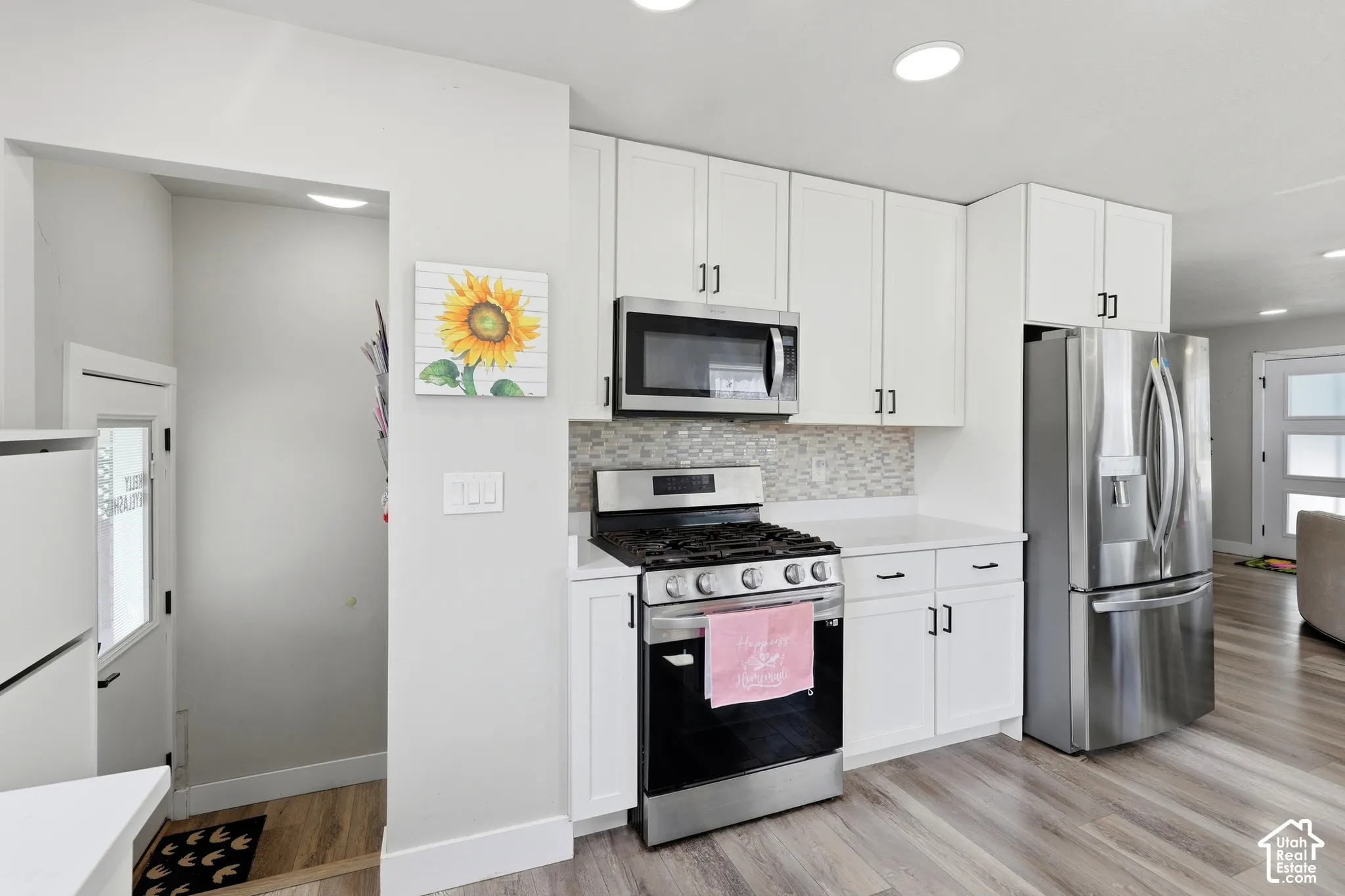 Kitchen featuring white cabinetry, stainless steel appliances, mosaic tile backsplash, white countertops, and wood-finish flooring