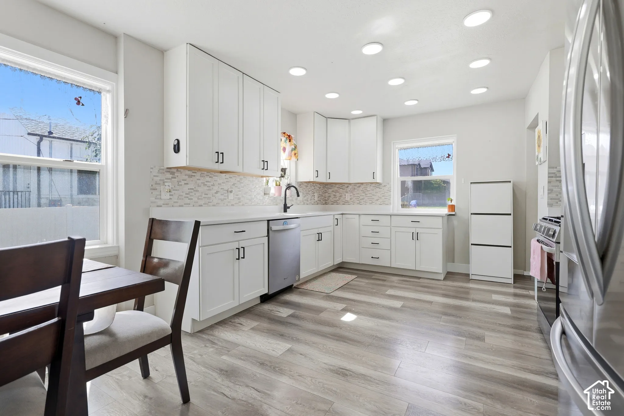 Kitchen featuring white cabinetry, light-toned wood-finish flooring, a mosaic tile backsplash, recessed ceiling lighting, and stainless steel appliances