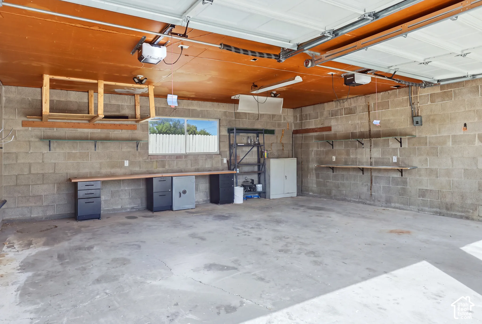 Concrete block walls, concrete flooring, overhead garage door, built-in workbench, and wall-mounted shelving