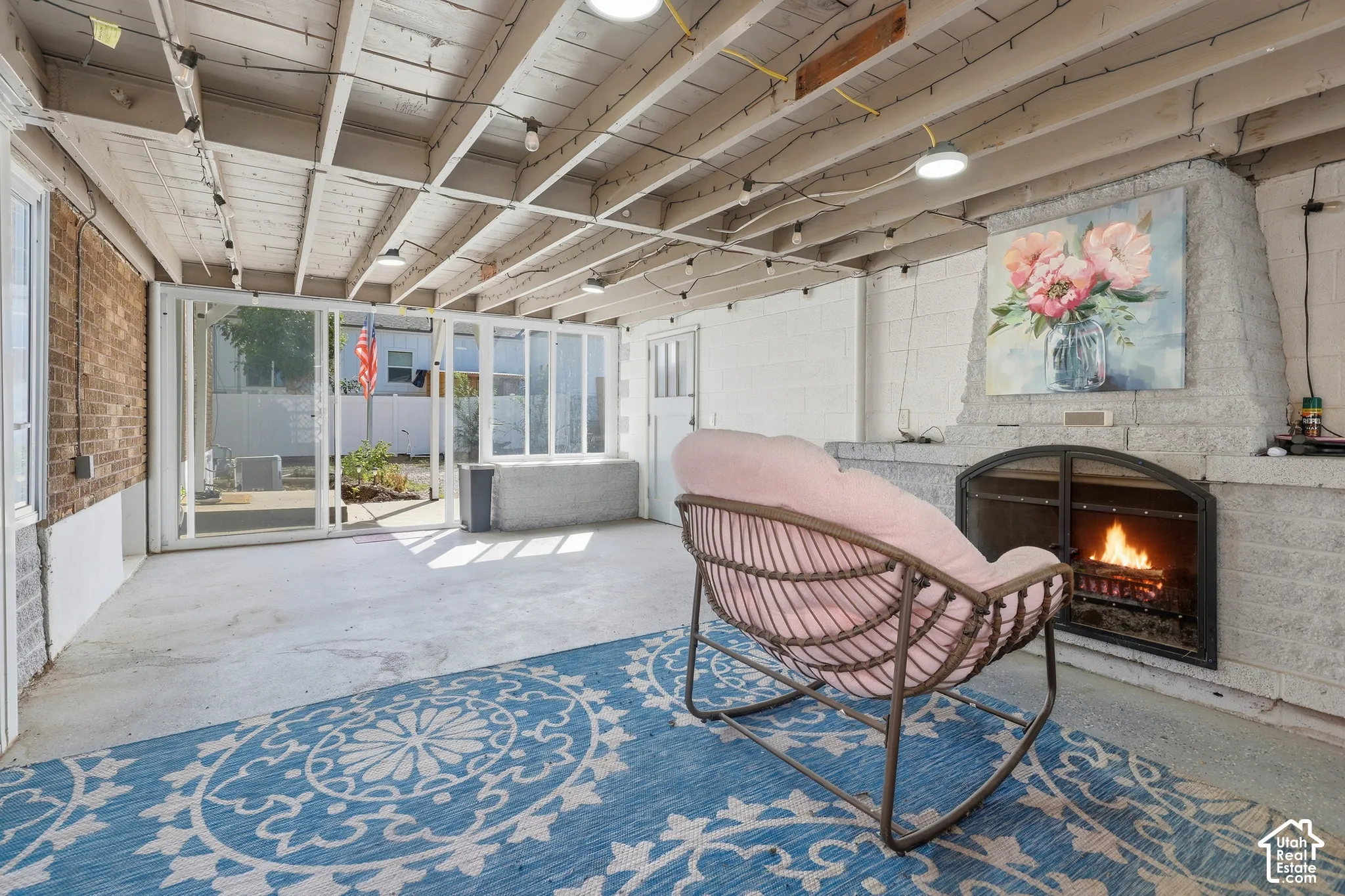 Concrete flooring, white exposed beam ceiling, brick accent wall, stone fireplace with hearth, and glass sliding door